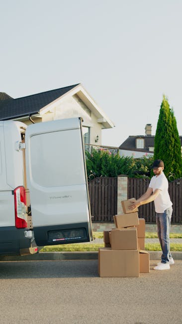 Two men are engaged in a home relocation process outside a residential property, with one man standing beside an open white van and the other sitting on the edge of the van's cargo area. The standing